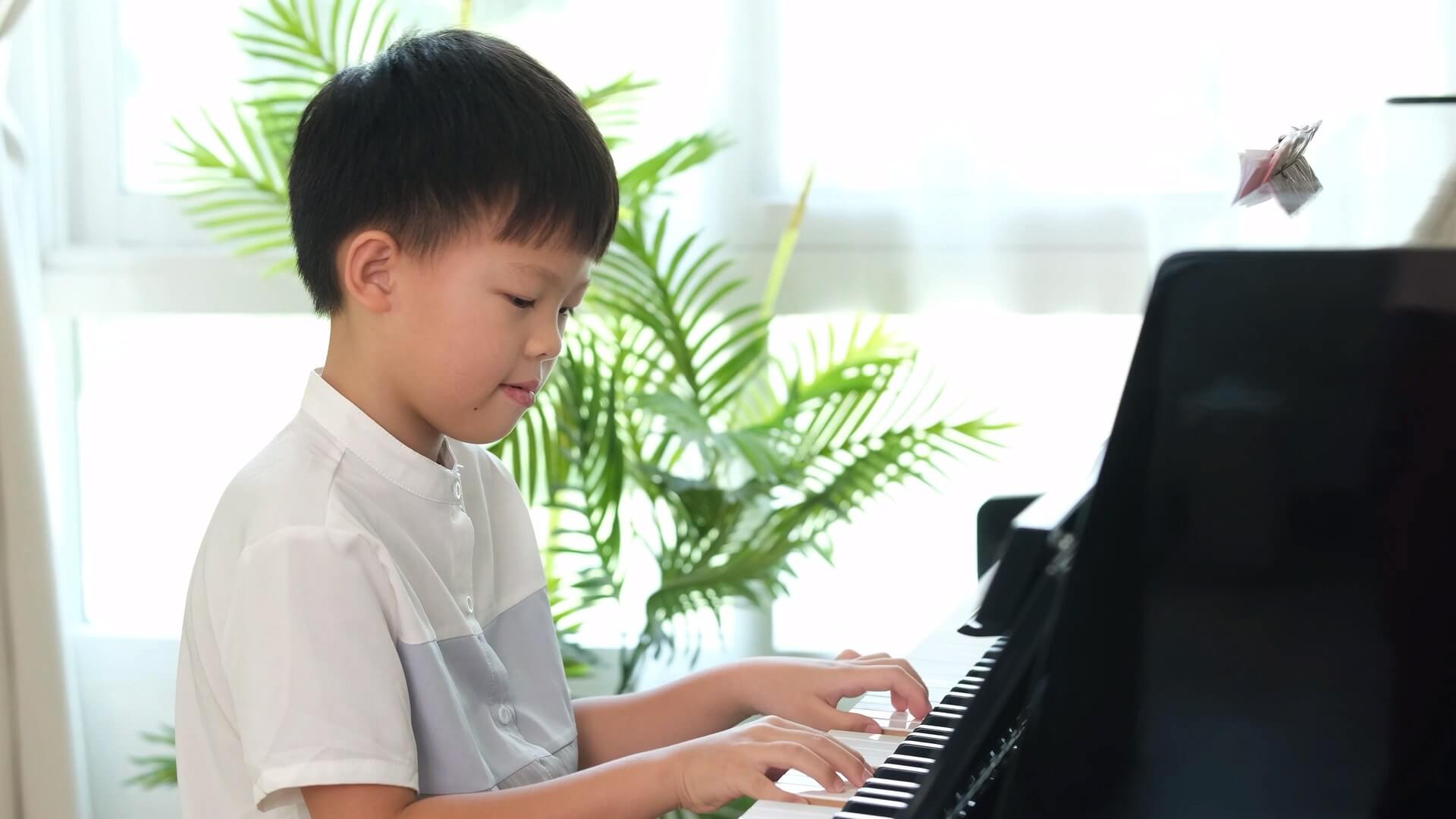 A young boy with black hair sitting at the piano, playing with both hands.
