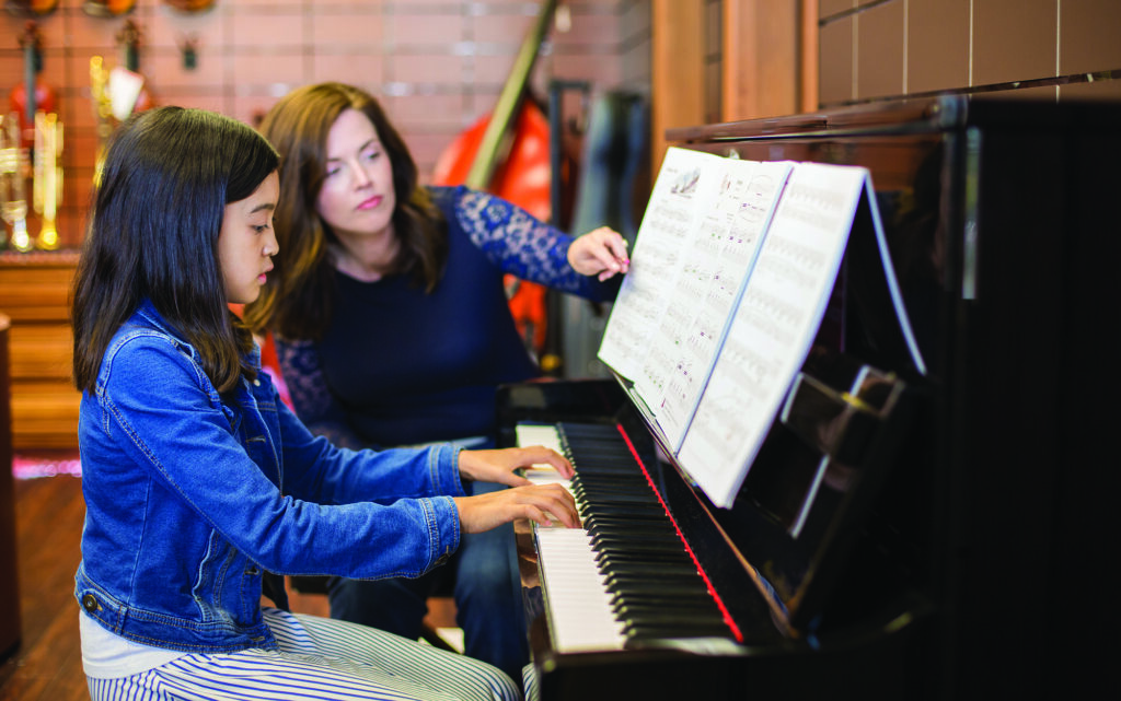Piano teacher is instructing her student.
