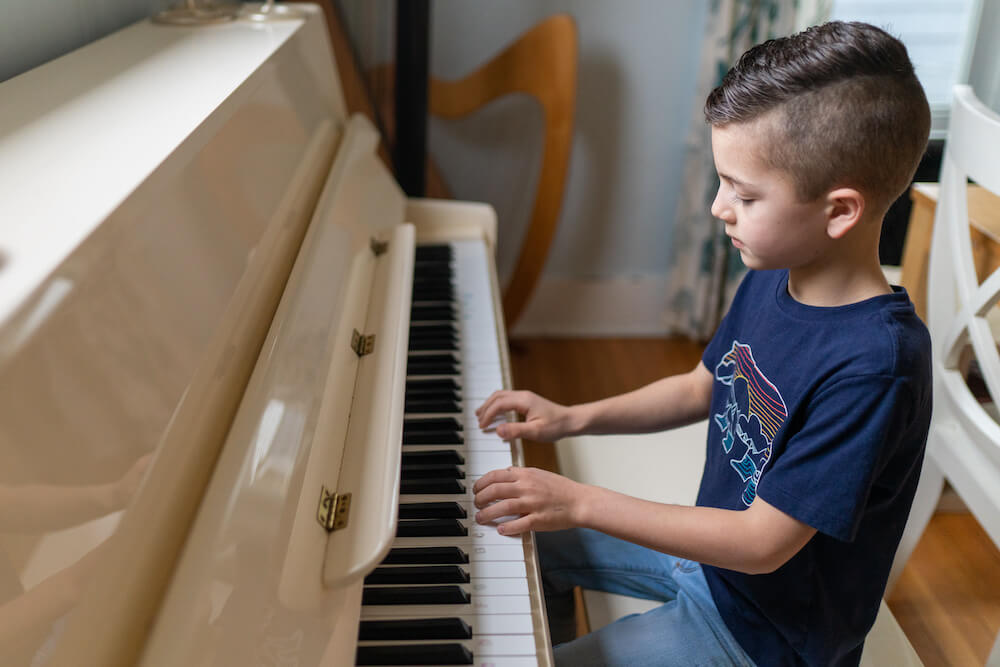 Boy playing at a white upright piano with good posture and technique